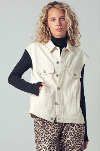 Woman wearing a cream vest over a black long-sleeve shirt and leopard print pants on a light gray background