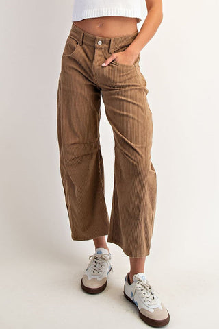 Woman wearing a white sleeveless top and brown pants on a plain background