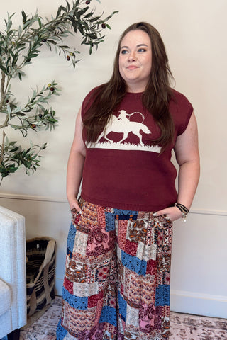 Woman wearing a burgundy t-shirt with a graphic design and patterned pants in a living room.