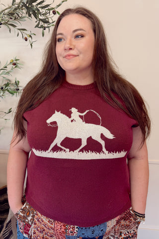 Woman wearing a maroon sweater with a white horse and rider design, standing indoors.