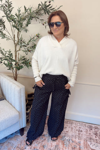 Woman in a white sweater and dark polka dot pants standing in a living room.