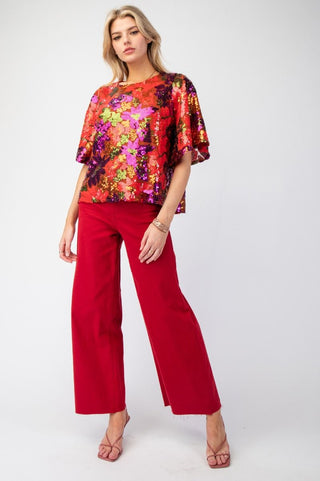 Woman wearing a colorful floral blouse and red pants on a white background