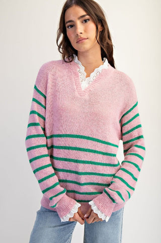 Woman wearing a pink sweater with green stripes on a plain background