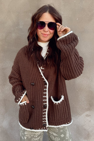 Woman wearing a brown knitted cardigan with white trim against a plain background
