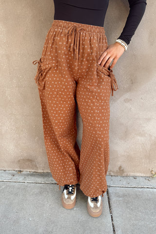 Person wearing brown polka dot pants against a beige wall.