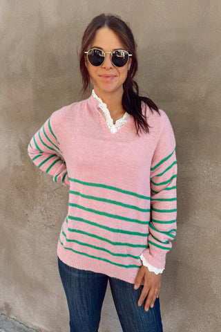Woman wearing a pink and green striped sweater against a plain wall