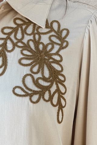 Beige blouse with gold embroidery on a neutral background