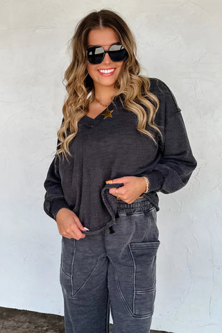 Woman wearing a dark gray outfit with sunglasses against a white wall