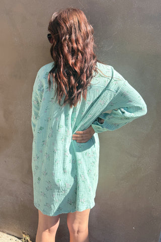 Person wearing a light green textured dress against a plain wall