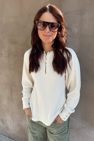 Woman wearing sunglasses and a white shirt against a gray wall