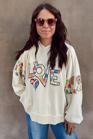 Person wearing a colorful 'LOVE' sweatshirt against a brown wall