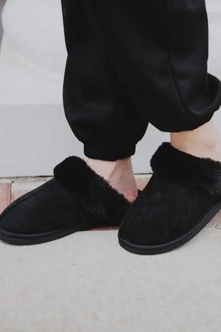 Black slippers with fuzzy texture worn indoors on a light-colored floor.
