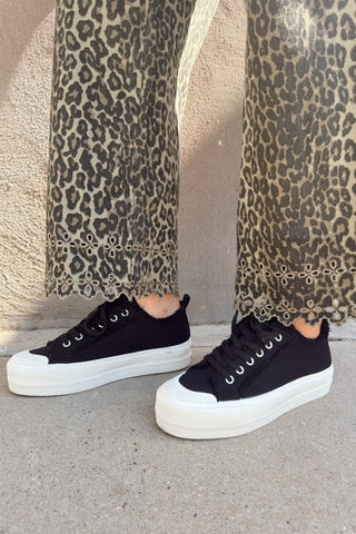 Black sneakers worn with leopard print pants on a neutral background