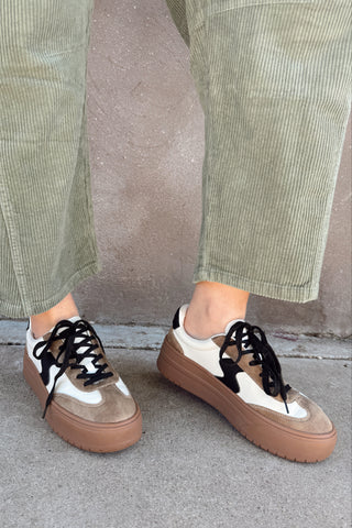 Person wearing brown and white sneakers with green pants against a neutral background