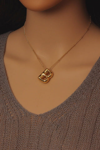 Gold necklace with a pendant on a mannequin wearing a brown sweater.