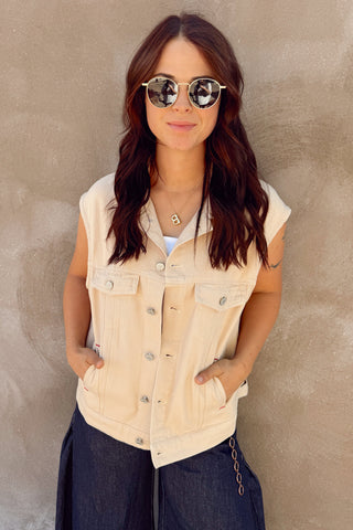 Woman wearing a beige sleeveless denim vest against a beige wall