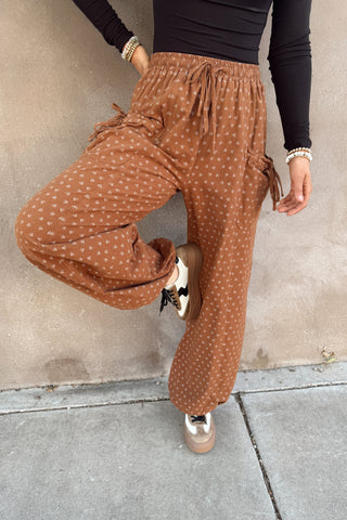 Person wearing brown polka dot pants against a concrete wall.