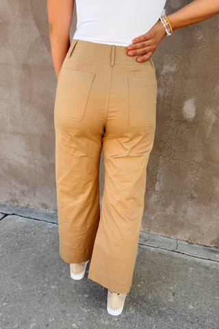 Person wearing beige pants and a white top against a brown wall.