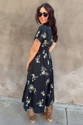 Woman wearing a black floral dress against a beige wall.
