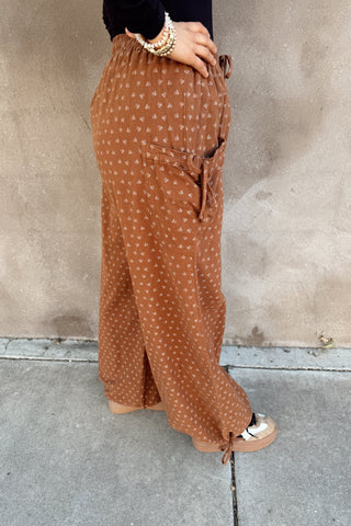 Person wearing brown patterned pants standing against a concrete wall.