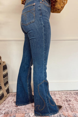 Person wearing blue flared jeans with a white wall and textured rug in the background