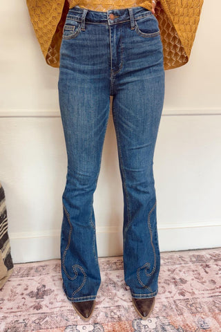 Blue flared jeans with decorative stitching on a patterned rug.