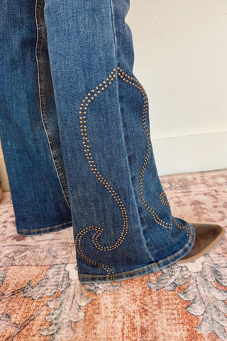 Close-up of blue jeans with decorative stitching on a patterned rug.