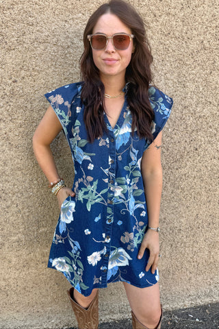 Woman wearing a blue floral dress against a beige wall