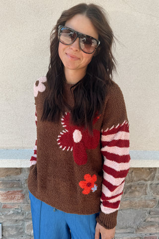 Person wearing a brown sweater with floral patterns against a beige wall.