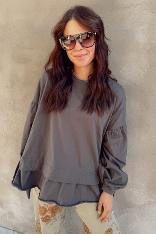 Woman wearing a gray sweatshirt and patterned pants against a beige wall