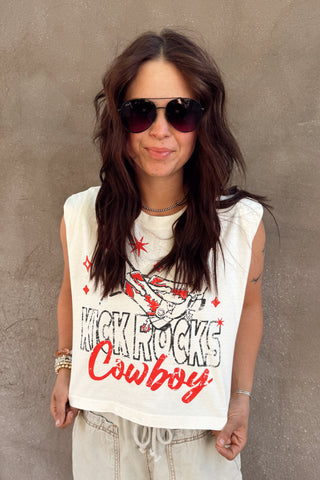 Woman wearing a sleeveless shirt with text and sunglasses against a concrete wall.