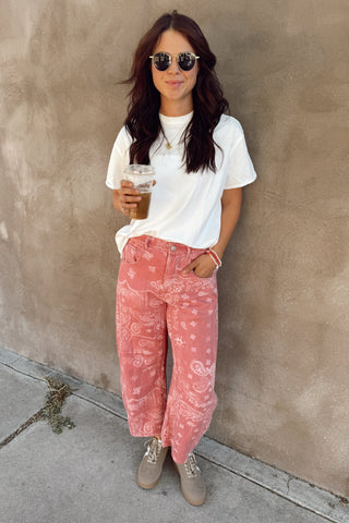 Woman wearing a white t-shirt and pink acid-wash jeans, standing against a beige wall.