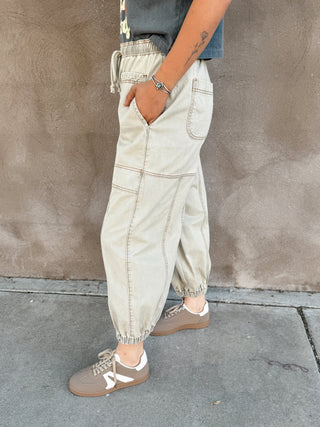 Person wearing light-colored cargo pants and brown shoes against a concrete wall.