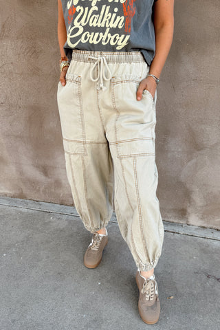Person wearing a graphic t-shirt and light-colored pants standing against a textured wall.