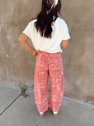 Person wearing a white t-shirt and pink tie-dye pants standing against a beige wall.