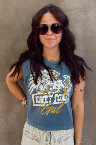 Woman wearing a 'Honky Tonk Gal' tank top against a textured wall.