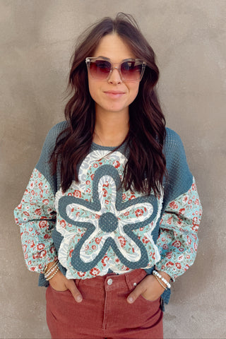 Woman wearing a floral sweater with a large blue flower design against a plain background