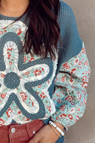 Woman wearing a floral sweater with a large central flower design against a plain background