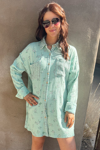 Woman wearing a light green dress with a subtle pattern against a gray wall.
