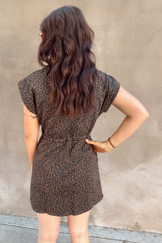 Person wearing a brown patterned dress against a beige wall.