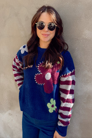 Woman wearing a colorful sweater with floral patterns against a plain background