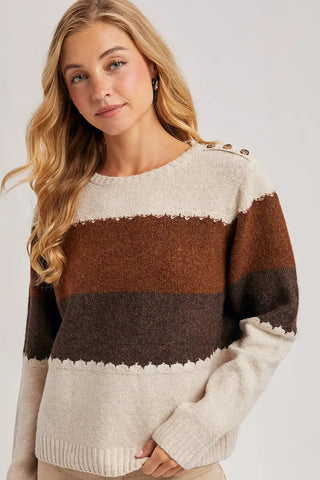 Woman wearing a striped sweater with beige, brown, and black colors on a plain background