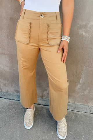 Person wearing beige pants and white top against a gray wall.