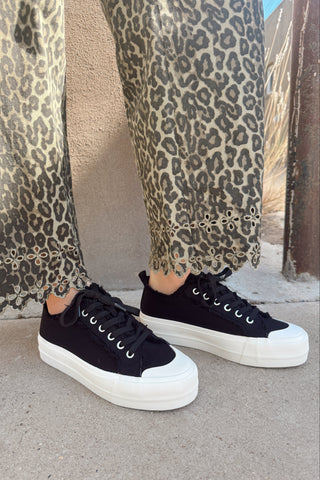 Person wearing black sneakers with white soles and leopard print pants.
