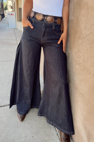 Person wearing wide-leg jeans and a white top, standing against a wall.
