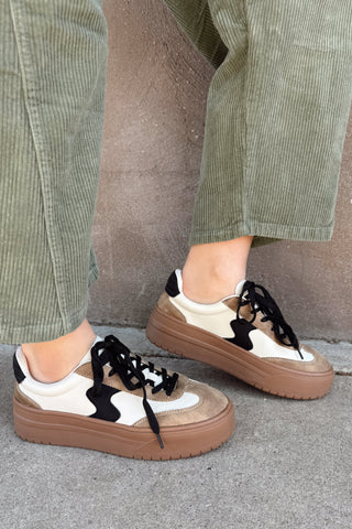Person wearing brown and white sneakers with black accents on a concrete surface.