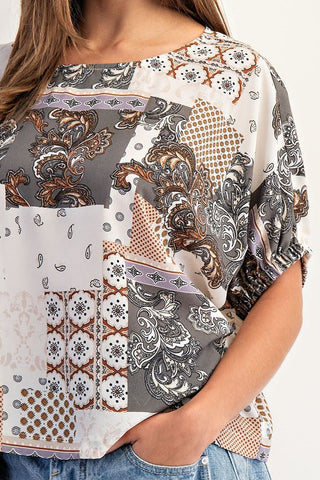 Woman wearing a patterned top and jeans on a plain background