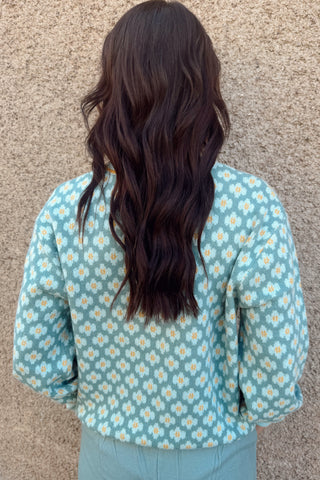 Person wearing a light blue floral patterned shirt against a beige wall