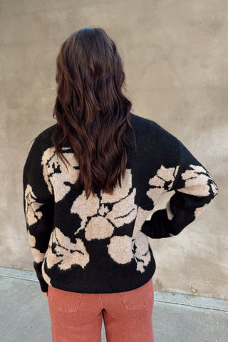 Person wearing a black floral sweater against a beige wall