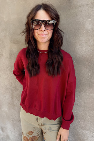 Person wearing a red sweater and sunglasses against a plain background